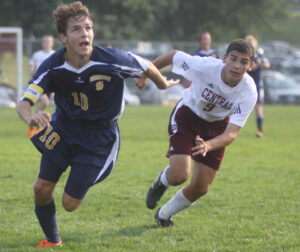 Two young men running for the soccer ball on the outdoor soccer field